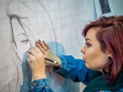 Student drawing a portrait with pencil on large graph paper on wall at the College of the Arts.